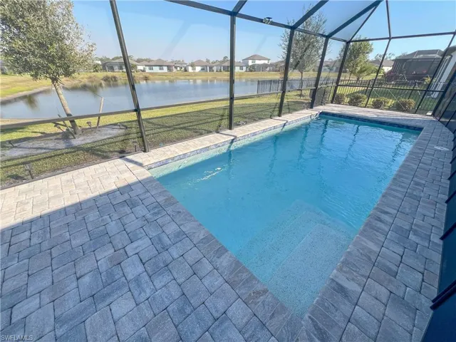 Pool featuring glass enclosure, a water view, a lawn, and a patio