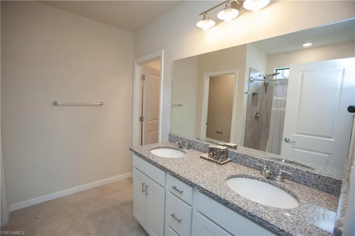 Bathroom featuring baseboards, a tile shower, double vanity, and a sink