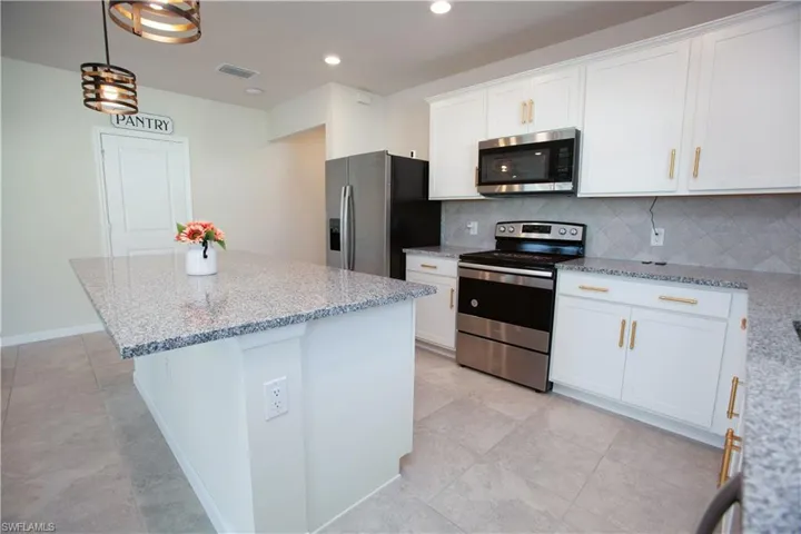 Kitchen with appliances with stainless steel finishes, backsplash, a center island, white cabinetry, and light stone countertops