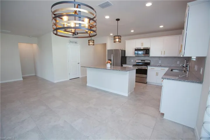 Kitchen with appliances with stainless steel finishes, backsplash, stone countertops, a center island, and a chandelier