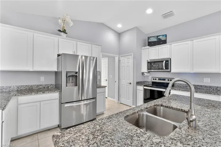 Kitchen featuring stainless steel appliances, white cabinets, lofted ceiling, light tile patterned floors, and light stone counters