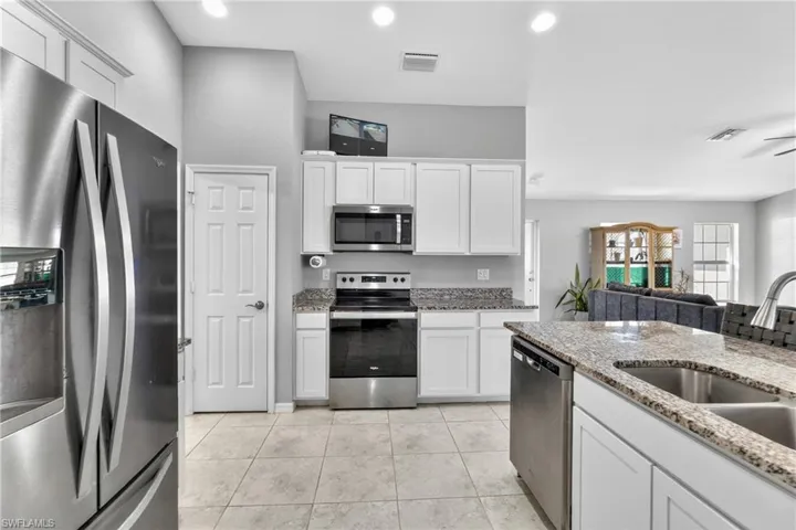 Kitchen with stainless steel appliances, white cabinetry, light stone countertops, open floor plan, and light tile patterned floors
