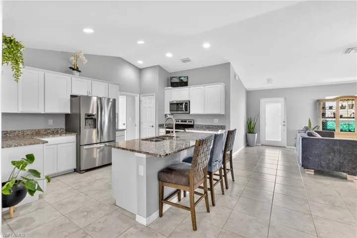 Kitchen with stainless steel appliances, a breakfast bar area, dark stone countertops, white cabinets, and lofted ceiling