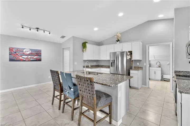 Kitchen with white cabinetry, light stone countertops, stainless steel appliances, light tile patterned floors, and lofted ceiling