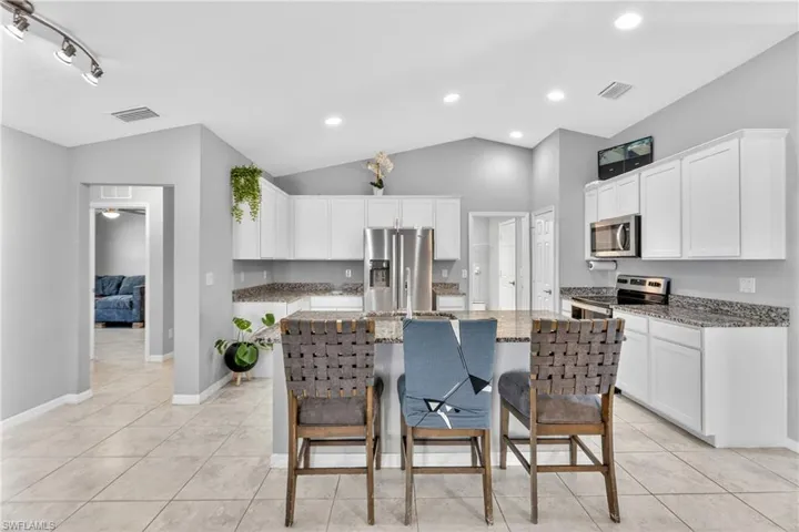Kitchen with light stone countertops, a kitchen bar, white cabinetry, stainless steel appliances, and a kitchen island with sink