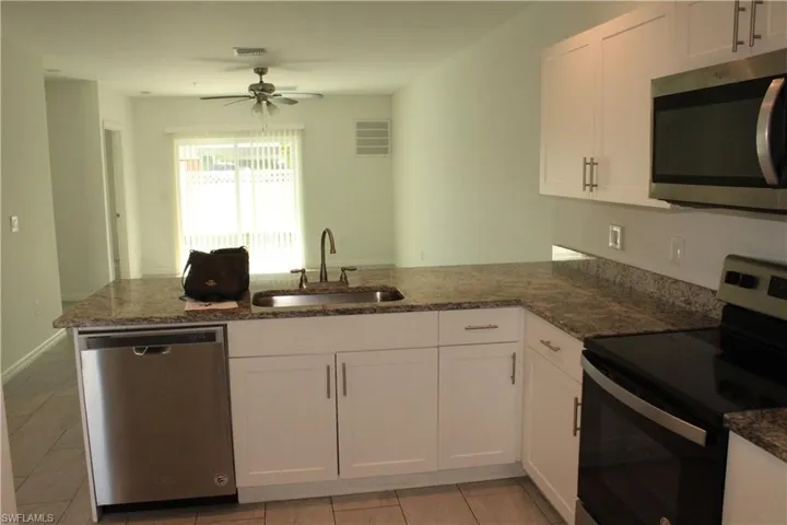 Kitchen featuring stainless steel appliances, a peninsula, white cabinets, dark stone counters, and ceiling fan