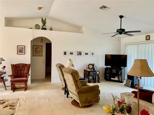 Carpeted living room featuring ceiling fan and vaulted ceiling