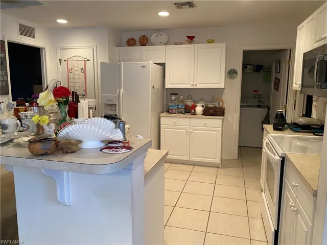 Kitchen featuring white cabinetry, a kitchen breakfast bar, washer / clothes dryer, white appliances, and light tile patterned floors