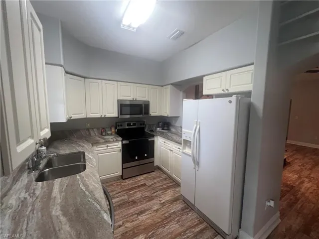 Kitchen featuring cream-colored cabinetry, stone-patterned countertops, wood-finish flooring, and stainless steel appliances