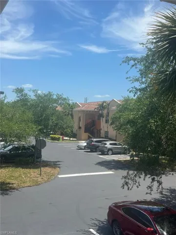 Exterior grounds featuring paved asphalt parking, mature landscaping, and stucco building facade with tile roofing