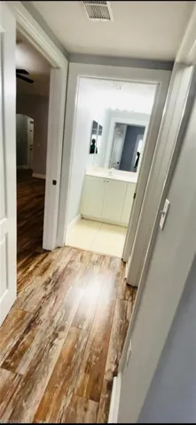 Wood-finish flooring throughout the hallway, bathroom vanity with integrated cabinetry, and ceramic tile bathroom flooring