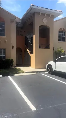 Stucco exterior featuring arched architectural elements, decorative gable detailing, a covered staircase with metal railing, and dedicated paved parking