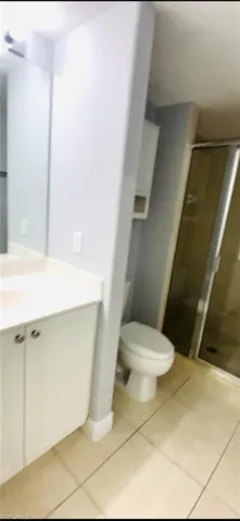 Bathroom featuring a white vanity cabinet, solid-surface countertop with an integrated sink, full-height wall mirror, toilet, and a glass-enclosed shower with tile flooring