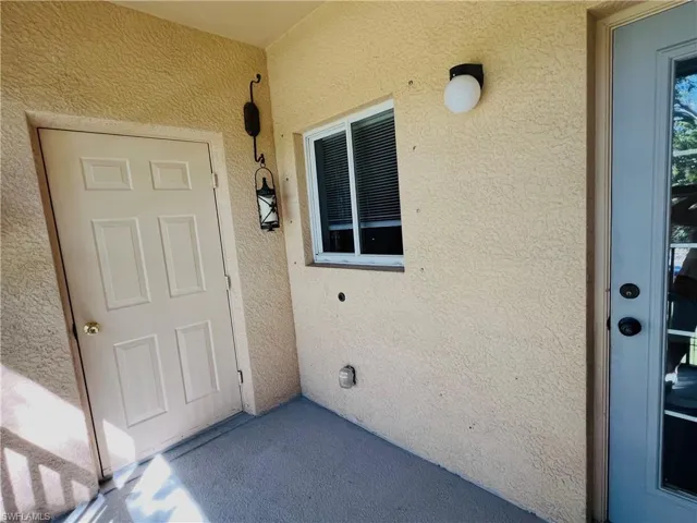 Covered patio entry featuring textured stucco exterior walls, sliding window, exterior wall-mounted globe lighting, and decorative metal lantern-style fixture