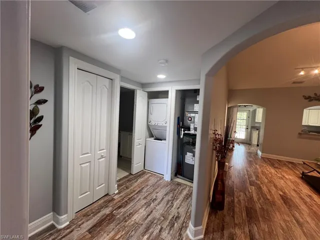 Laundry area featuring a stacked washer and dryer unit, wood-finish flooring, recessed lighting, and arched architectural openings