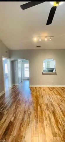 Wood-finish flooring, vaulted ceilings, arched architectural detailing, and built-in pass-through window with ledge