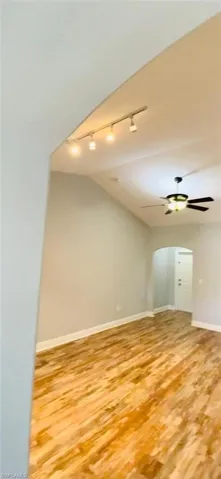 Vaulted ceilings, wood-finish flooring, adjustable track lighting, and a ceiling fan with integrated light fixture