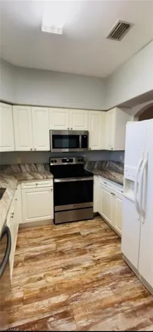 Kitchen featuring white cabinetry, wood-finish flooring, stainless steel appliances, and patterned stone-finish countertops