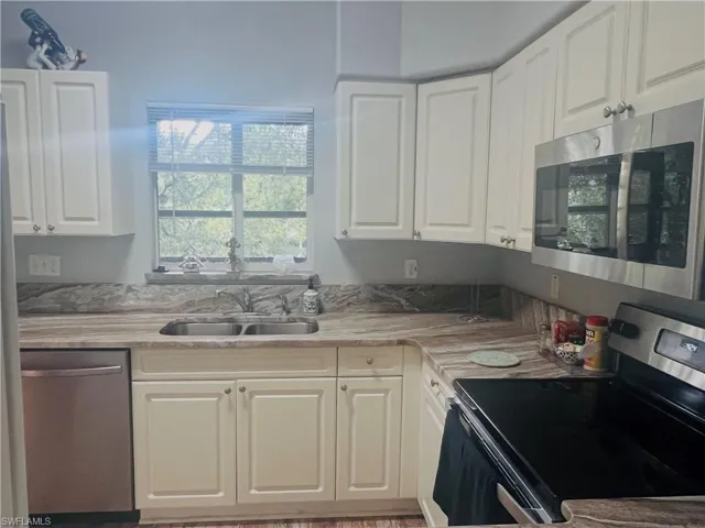 Kitchen featuring off-white cabinetry, stone-patterned countertops with matching backsplash, stainless steel dishwasher, and built-in stainless steel microwave