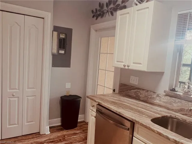 Utility area featuring white shaker-style cabinetry, natural stone-finish countertops, wood-finish flooring, stainless steel dishwasher, and a glass-paneled door