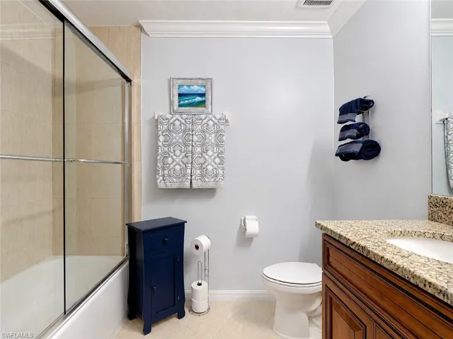Bathroom featuring a built-in tub with sliding glass doors, tan tiled surround, and crown molding