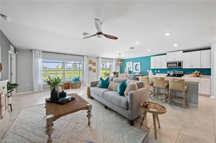 Open-concept living area featuring light-toned tile flooring, a contemporary ceiling fan, and large windows