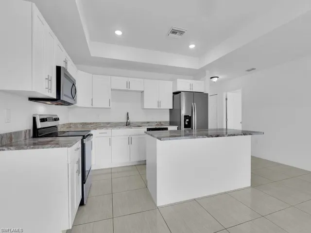 Kitchen with stainless steel appliances, white cabinetry, a center island, a tray ceiling, and recessed lighting