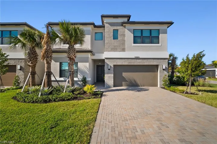 View of front facade with stucco siding, decorative driveway, a front lawn, and an attached garage