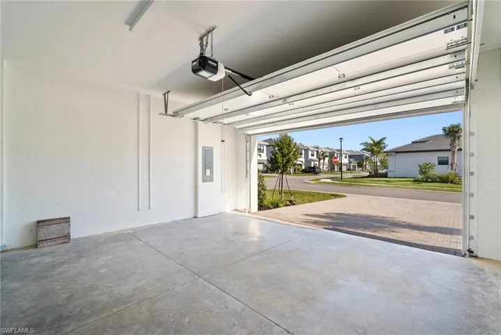 Garage with a residential view, a garage door opener, electric panel, and decorative driveway