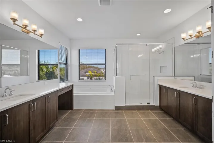 Bathroom with a garden tub, two vanities, a stall shower, dark tile patterned flooring, and recessed lighting