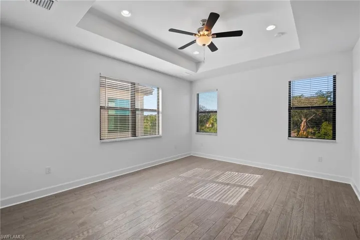 Unfurnished room with light wood-type flooring, plenty of natural light, a raised ceiling, recessed lighting, and ceiling fan