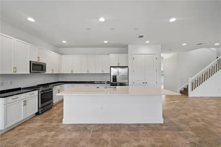 Kitchen featuring stainless steel appliances, white cabinets, an island with sink, recessed lighting, and dark stone countertops