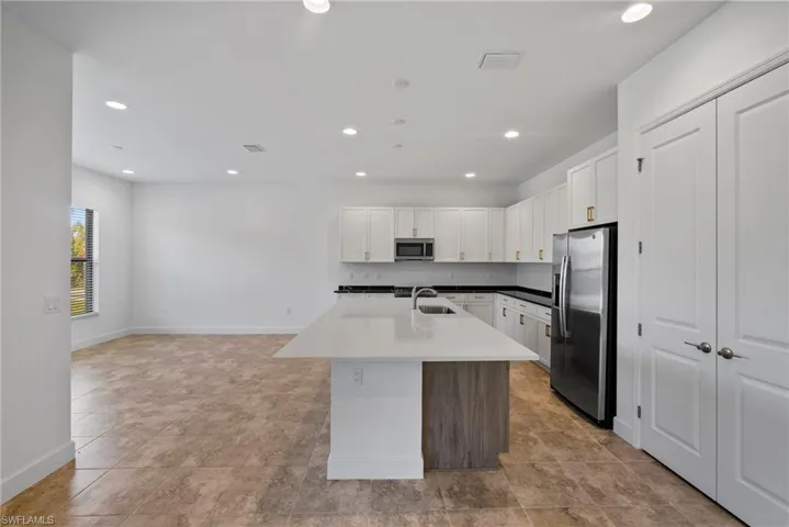 Kitchen with stainless steel appliances, white cabinets, recessed lighting, an island with sink, and open floor plan