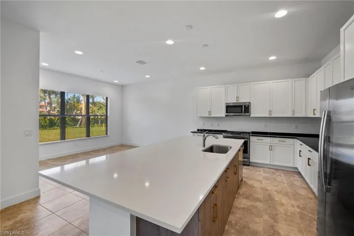 Kitchen with appliances with stainless steel finishes, white cabinets, recessed lighting, an island with sink, and dark stone counters