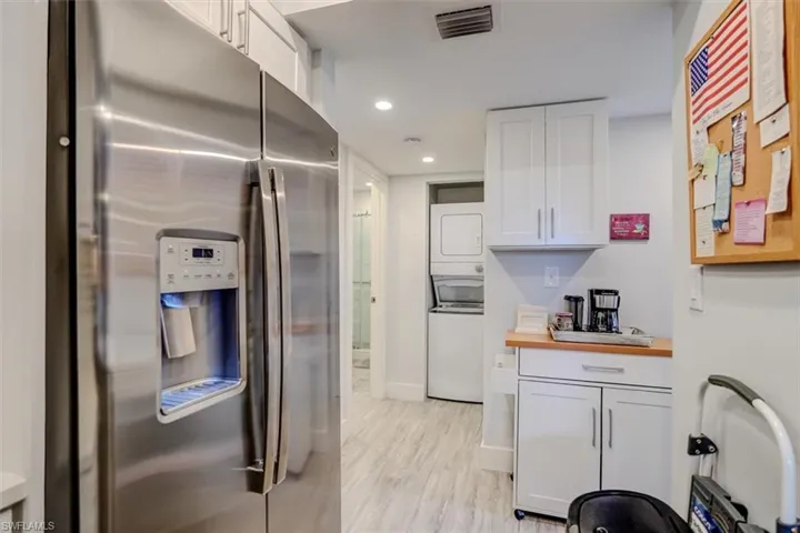 Kitchen featuring stainless steel refrigerator with ice dispenser, light wood-type flooring, stacked washer / dryer, and white cabinets