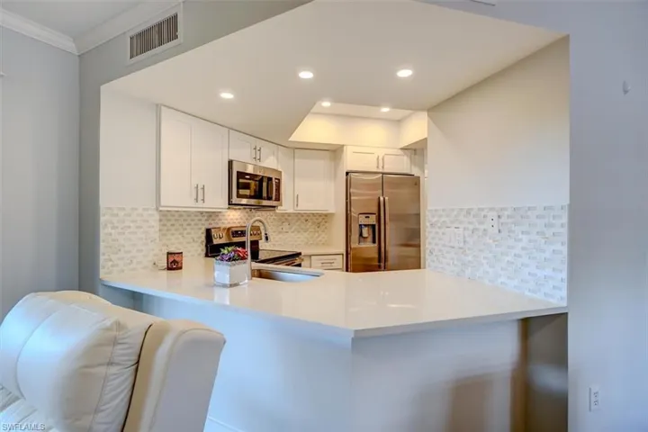 Kitchen featuring backsplash, kitchen peninsula, white cabinets, and stainless steel appliances