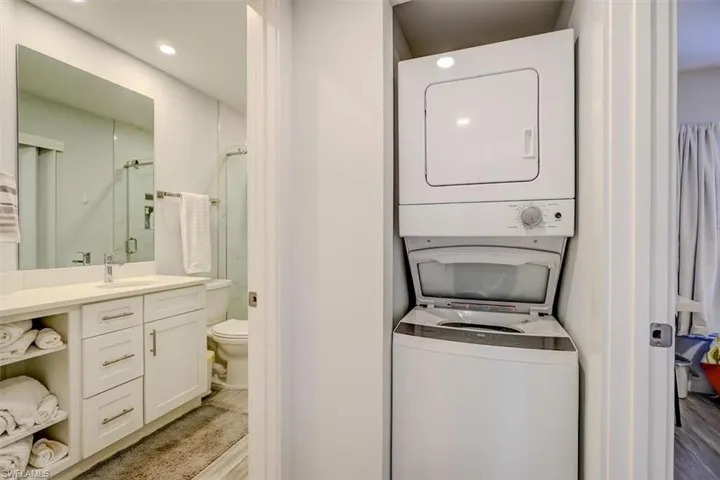 Clothes washing area featuring sink, stacked washer and dryer, and light wood-type flooring