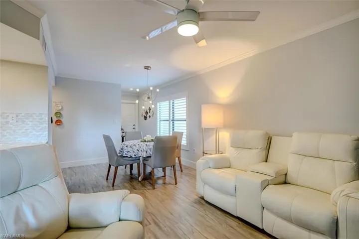 Living room with ceiling fan with notable chandelier, light hardwood / wood-style floors, and crown molding