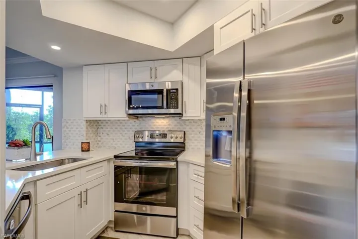 Kitchen with backsplash, white cabinetry, sink, and stainless steel appliances