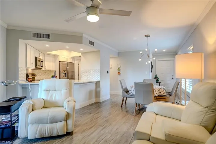 Living room with crown molding, light hardwood / wood-style floors, and ceiling fan with notable chandelier