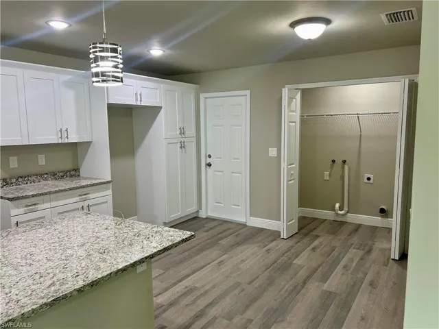 Kitchen with light hardwood / wood-style floors, white cabinets, light stone countertops, and decorative light fixtures
