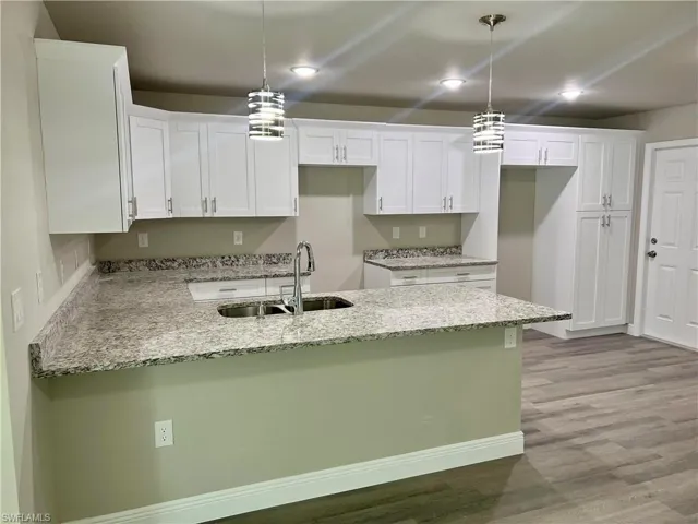 Kitchen featuring white cabinets, light stone counters, sink, light hardwood / wood-style floors, and decorative light fixtures