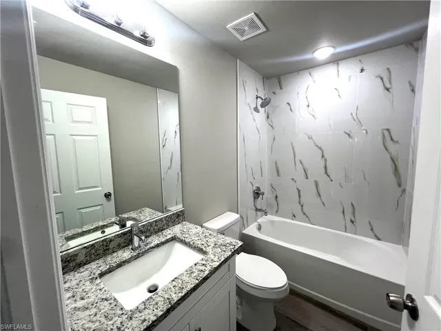 Full bathroom with toilet, tiled shower / bath, hardwood / wood-style flooring, and vanity