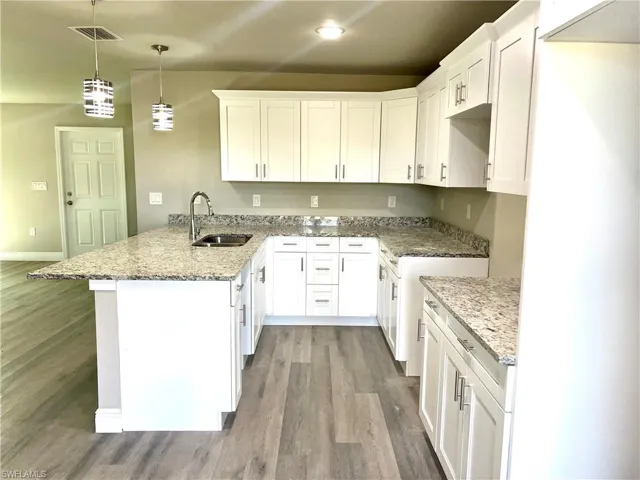 Kitchen featuring kitchen peninsula, white cabinets, sink, and decorative light fixtures
