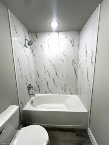 Bathroom with toilet, tiled shower / bath, and hardwood / wood-style floors