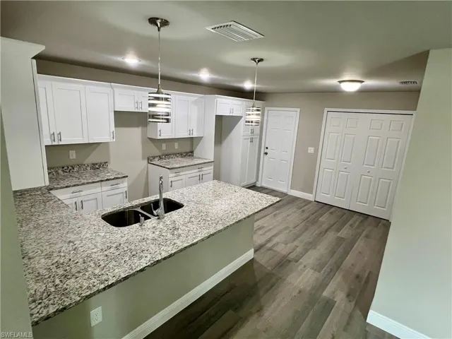 Kitchen featuring sink, kitchen peninsula, pendant lighting, white cabinets, and dark wood-type flooring