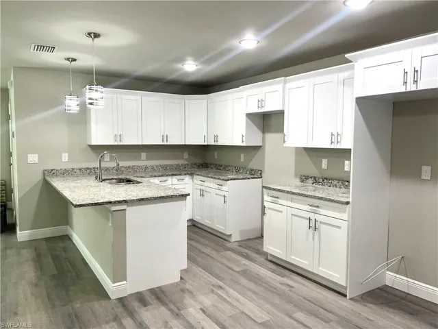 Kitchen featuring white cabinets, light stone countertops, light hardwood / wood-style flooring, sink, and decorative light fixtures