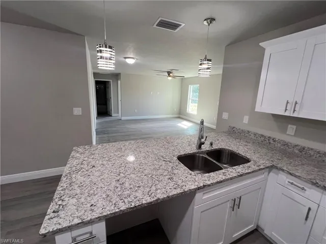 Kitchen with sink, white cabinetry, pendant lighting, and dark hardwood / wood-style flooring