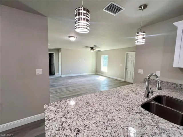 Kitchen featuring sink, light stone counters, pendant lighting, and dark hardwood / wood-style flooring