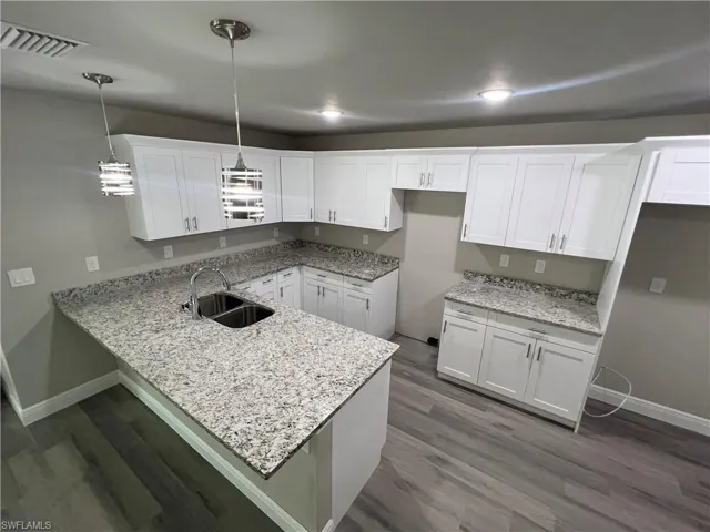 Kitchen featuring white cabinetry, sink, hanging light fixtures, and dark hardwood / wood-style floors